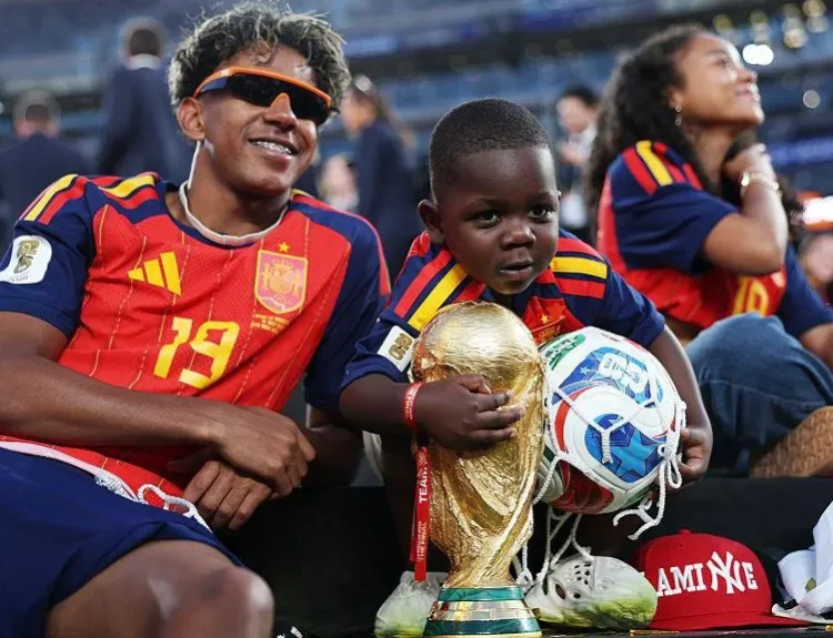 Lamine Yamal smiling alongside his 3-year-old brother Kenye on the pitch at the New York New Jersey Stadium after winning the 2026 World Cup.