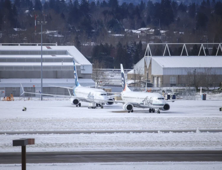 An Alaska Airlines passenger jet sitting on a snow-covered runway during winter operations.